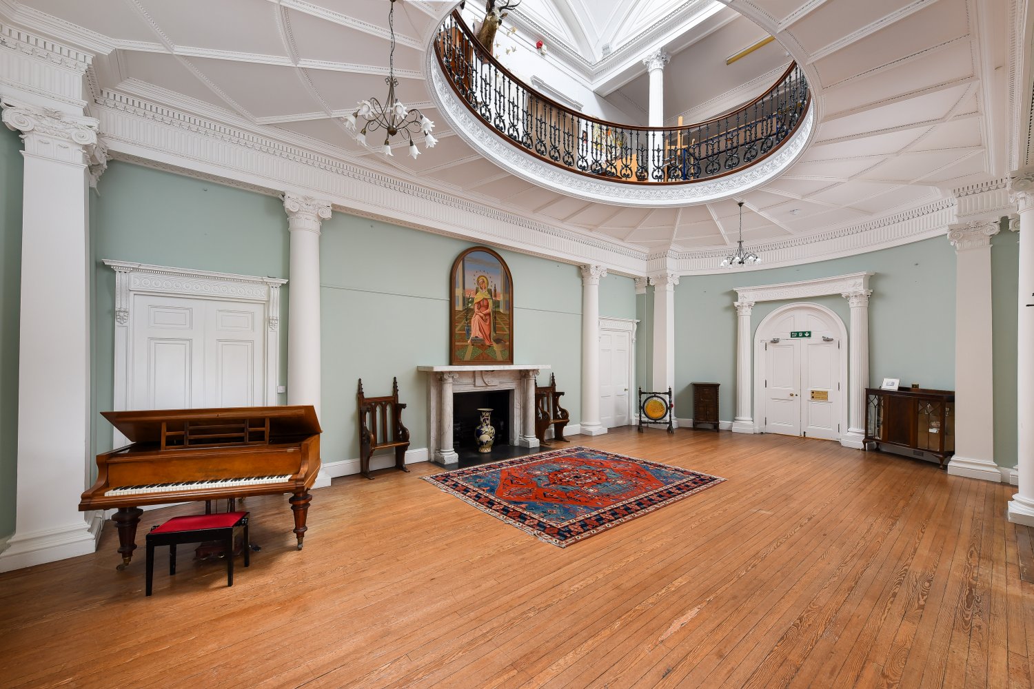 Grand hall interior with a piano, rug, and circular balcony.